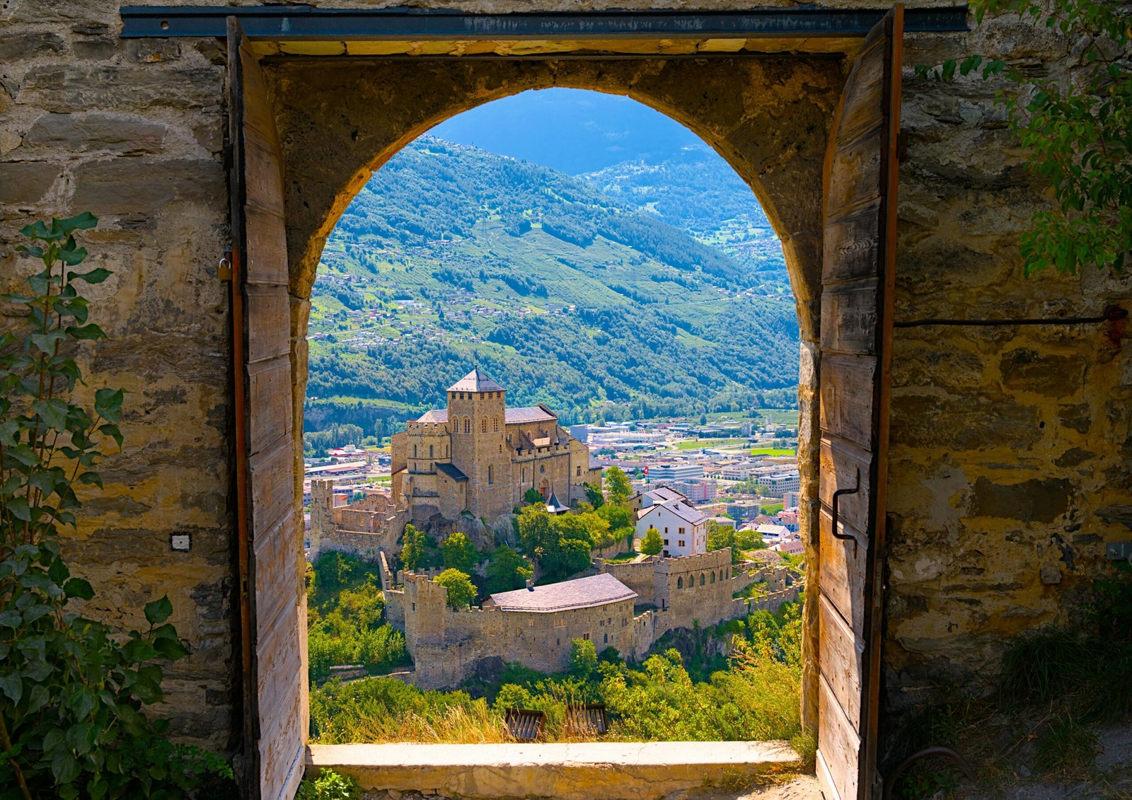 Stunning view of Sion, Switzerland, through Basilica door frame showcasing landscape and architecture.
